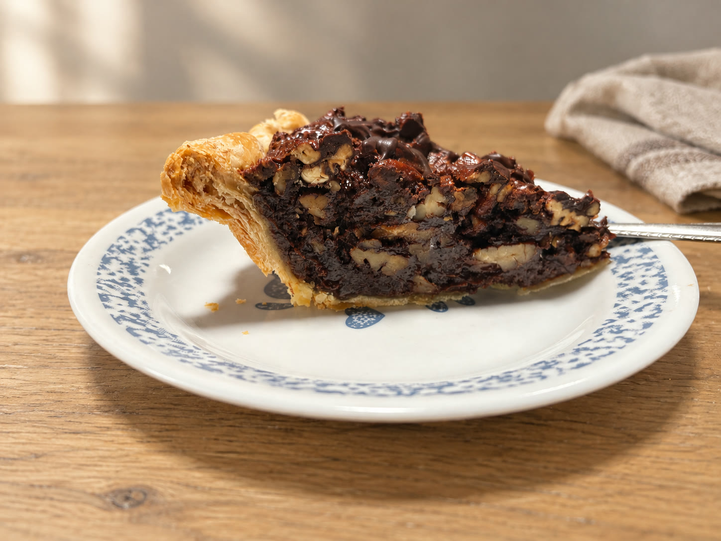 Rick’s chocolate pecan pie, with a flaky golden crust, on a blue-and-white plate. Background styled with AI.